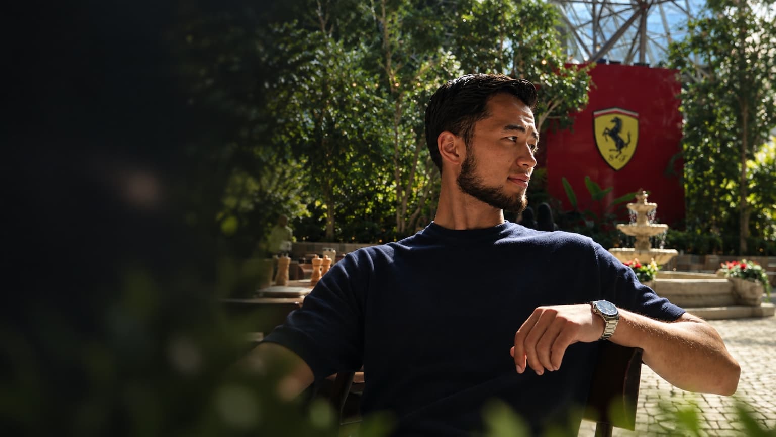 Bek outdoors, looking off to the side, backlit by afternoon sun with greenery around him