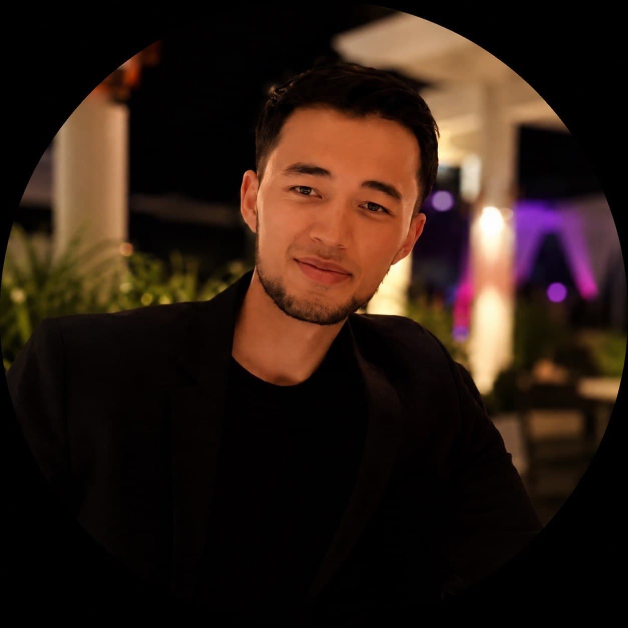 Bek, wearing a black blazer, photographed outdoors in the evening